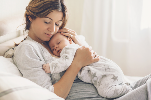 A mother cradling her sleeping baby in bed.